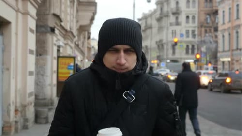 Front View Of Young Man Walking Down The City Street And Drinking Coffee