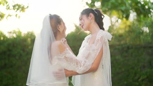 4K Портрет азиатской лесбийской пары в свадебном платье, держащейся за руки, идущей вместе по саду.
