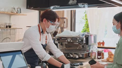 Asian customer wear mask due to Covid-19 pandemic, receive drink from waiter on coffee bar counter.
