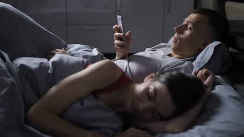 Man Looking at Phone while Woman Sleeping