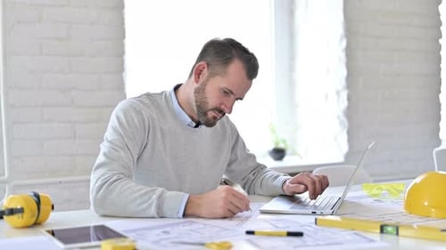 Junger Architekt mit Laptop erledigt Papierkram im Büro