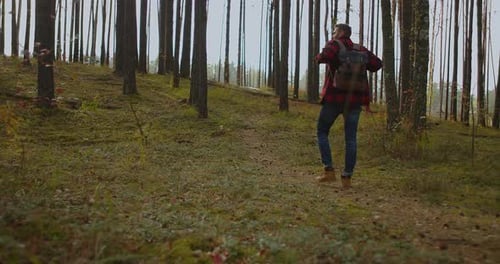 A Young Man Walks Uphill From the Forest in Autumn in Slow Motion with a Backpack. A Hipster Man in