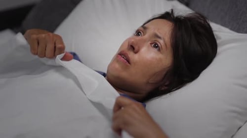 Mulher assustada se escondendo debaixo do cobertor