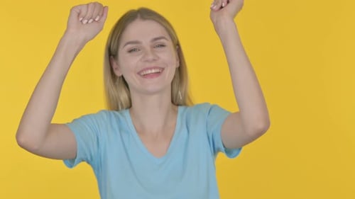 Enthusiastic Blonde Woman Dancing on Yellow Background
