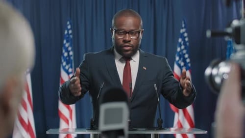 Man Giving Speech Behind Podium with American Flags