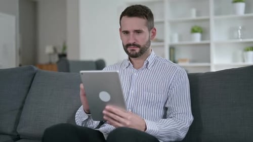 Man Cheers While Using Tablet on Couch