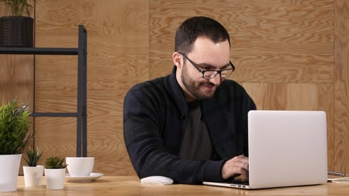 Junger bärtiger Mann trinkt Kaffee oder Tee, während er am Laptop arbeitet.