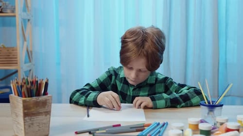 Child Draws and Erases at Table with Art Supplies