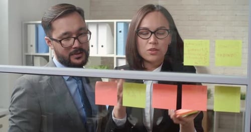 Professionals Collaborating with Sticky Notes on Glass Wall