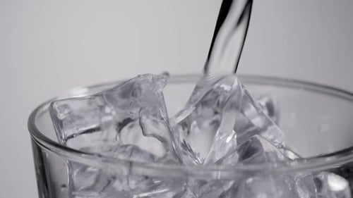 Close up slow motion water pouring into glass with ice cubes