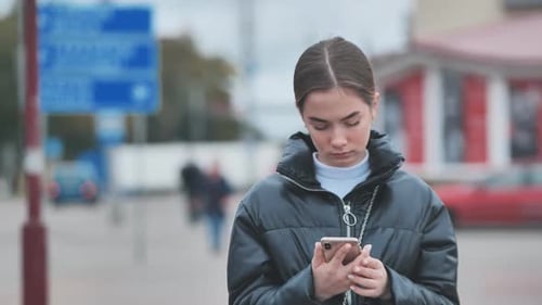 A Girl Walks Through Town and Looks Through Her Phone