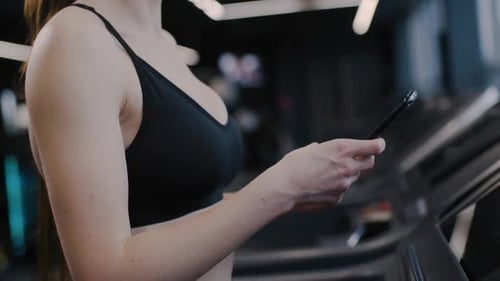 Gym Woman Athlete Walks on a Treadmill and Uses Smartphone Tracking Progress in Sports Aerobic