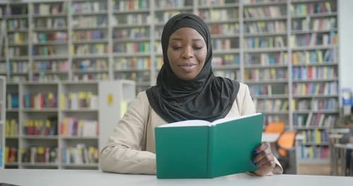 Positive Muslim Black Woman in Hijab Reads Book in Library