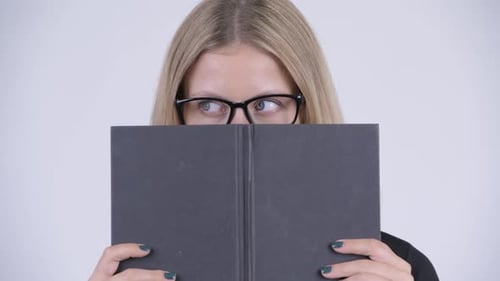 Visage de jeune femme nerd blonde timide couvrant le visage avec un livre