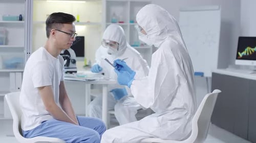 Arzt in Einweg-Overalls, der die Symptome des Patienten aufschreibt