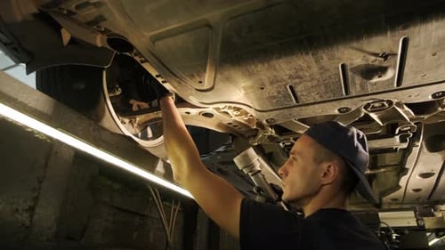 Mechanic Inspecting Underside of Car With Flashlight