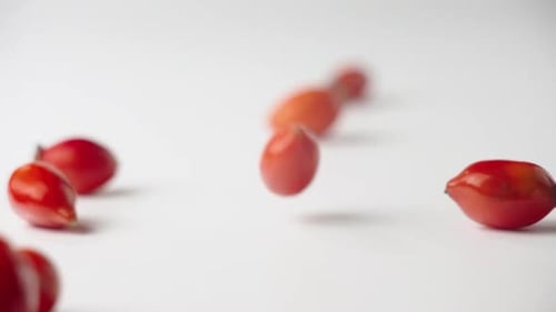 Shiny Red Rosehips Falling onto White Surface