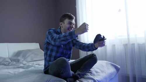 Mann hält Videospielkonsole in der Hand, steuert den Joystick und spielt zu Hause online