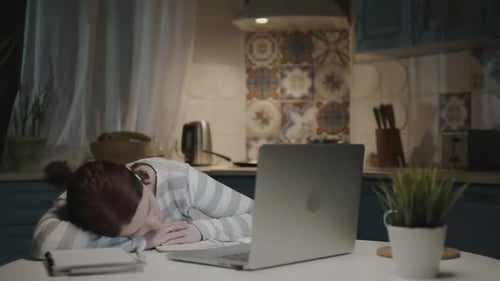 Woman In The Kitchen With Laptop. Tired Young Woman Sleeping On Desk Near Laptop