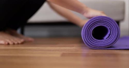 Woman unrolling purple yoga mat indoors