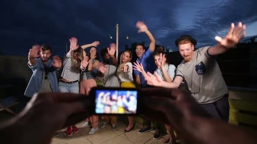 View of hands holding phone and filming happy group of friends waving to camera