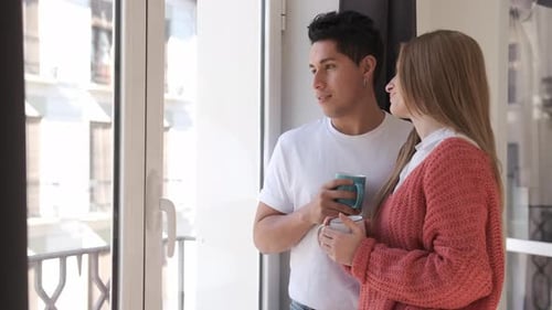 Casal relaxando e curtindo o tempo juntos enquanto toma um café e olha pela janela em casa.