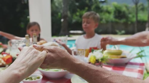 Family Holding Hands Around a Meal Outdoors