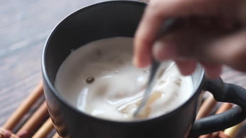 Hand stirs coffee in mug with spoon