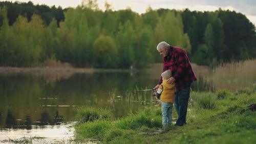 Little Boy is Learning to Fish on Lake Shore Loving Grandfather is Helping