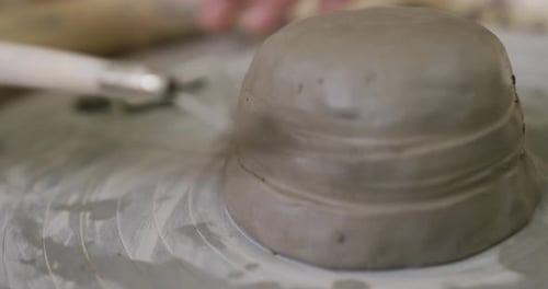 Vue rapprochée d'une potière utilisant un outil en boucle pour la finition de poteries dans un atelier de poterie
