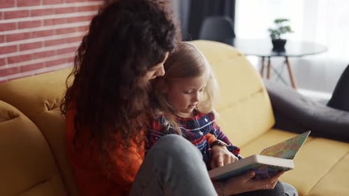 Woman and Child Reading Book Together on Sofa