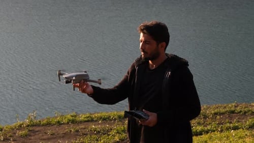 Young Man Prepping Drone Near Blue Tropical Lake