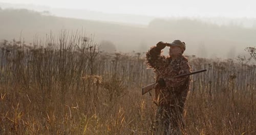 Hunter with Rifle Standing in the Field and Looking Around, Foggy Autumn Morning, Soft Sun Light