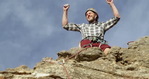 Climber cheering after reaching the top of cliff