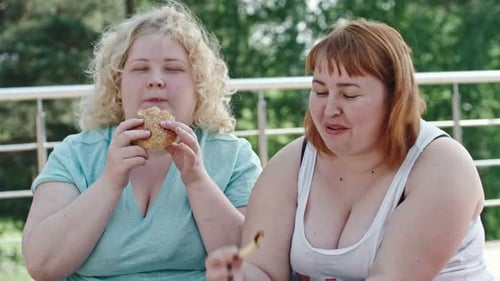 Two Young Women Eating Junk Food Outdoors