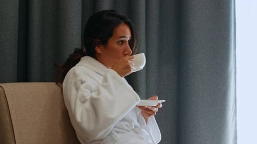 Uma bela jovem mestiça de pele escura senta-se perto da janela do hotel e bebe café.