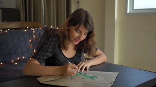Primer plano de una joven calígrafa escribiendo en una bolsa de papel usando la técnica de letras.
Ella