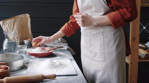 Woman Cracks Egg onto Flour Covered Table