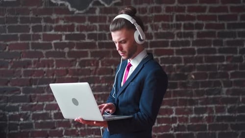 Handsome Young Businessman Headphone Using Laptop Standing Loft Office Red Brick Wall Background