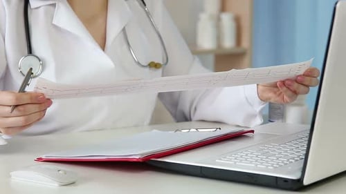 Kardiologin analysiert Elektrokardiogramm und schreibt Krankenakten auf
