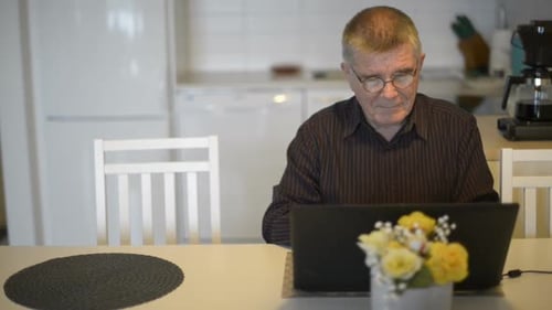 Homem sênior com óculos usando laptop na sala de jantar