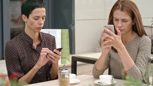 Women Using Phones at an Urban Cafe