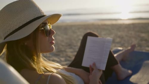young attractive woman sitting on a beautiful beach reading a book