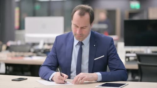 Businessman Writing on Paper in Office