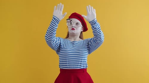 Female mime shows a pantomime wall, on an orange background. European actress mime in makeup
