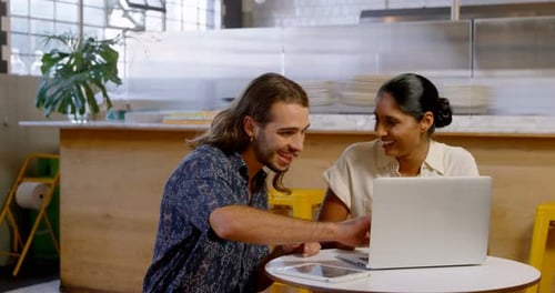Colleagues discussing over laptop in cafeteria