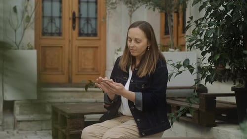 Smiling brunette woman uses her phone in the city. Pretty woman looking at her mobile phone