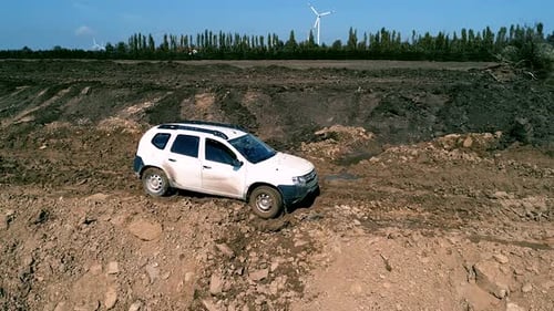 SUV Driving on Muddy Terrain with Windmills