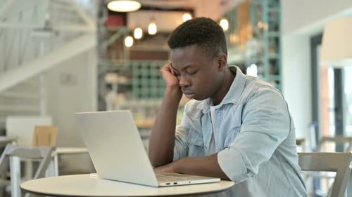 Sleepy Young African Man with Laptop Taking Nap in Cafe