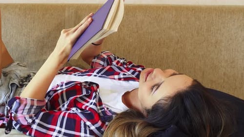 Woman Reads Book Lying on Sofa